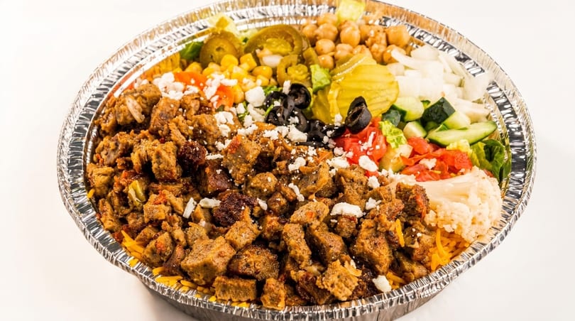 A large foil container filled with gyro meat, rice, chickpeas, salad, and various toppings.